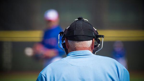 Photo of the back of the head of a baseball umpire with an out-of-focus pitcher in the background
